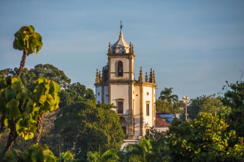 Historic colonial church tower with white walls and golden details surrounded by lush tropical vegetation in Rio de Janeiro