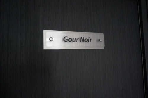 Plaque nominative Gour Noir sur porte texturée sombre à l'Hôtel Saint Roch, Saint Ybard