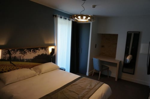 Chambre d'hôtel moderne à l'Hôtel Saint Roch à Saint Yrieix avec lit, bureau et éclairage contemporain