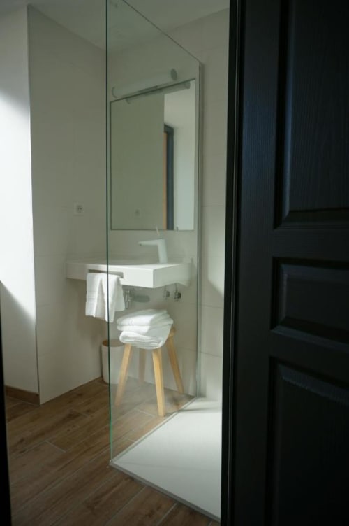 Salle de bain moderne de l'Hôtel Saint Roch avec douche vitrée, lavabo blanc, miroir et parquet
