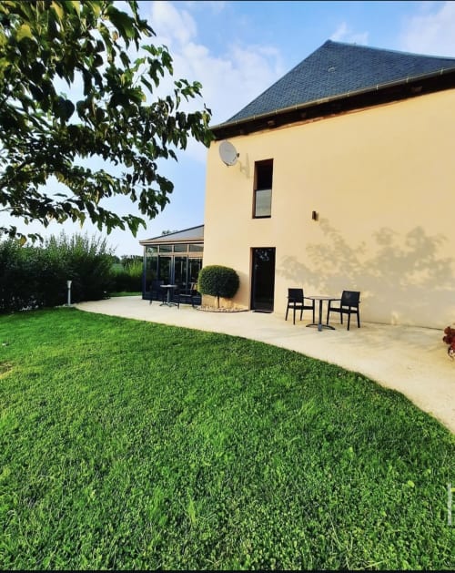 L'Hôtel Saint Roch à Saint-Ybard présente une façade jaune avec toit noir, terrasse aménagée et pelouse bien entretenue