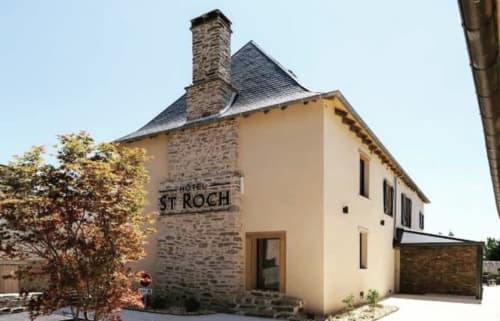 Façade extérieure de l'Hôtel Saint Roch à Saint Ybard, France avec cheminée en pierre et façade crème
