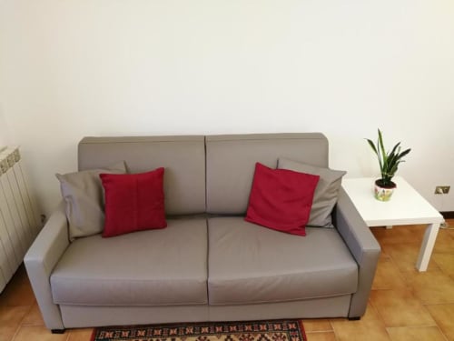 Gray sofa with red pillows in Carducci Apartment at THE V Collection, Turate, with white side table and potted plant