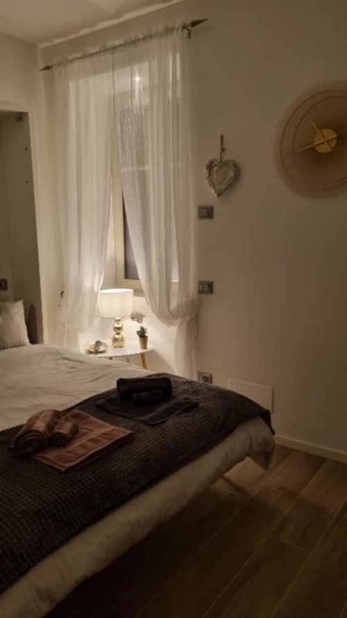 Camera accogliente a Maso Kreuzberg B&B a Trento con tende trasparenti, lampada comodino, orologio a muro e vista sul giardino