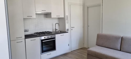 Modern kitchenette con mobili bianchi, fornello a gas e divano nell'appartamento Maso Kreuzberg a Trento