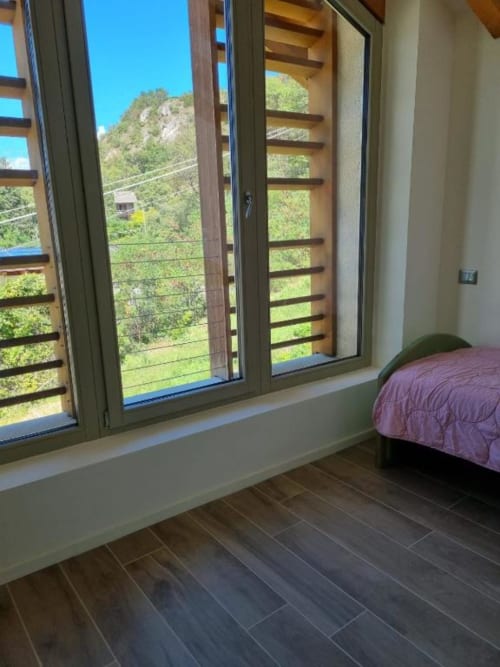 Camera da letto moderna a Maso Kreuzberg con vista montagna, porte in legno, pavimenti in piastrelle scure e letto con coperta viola