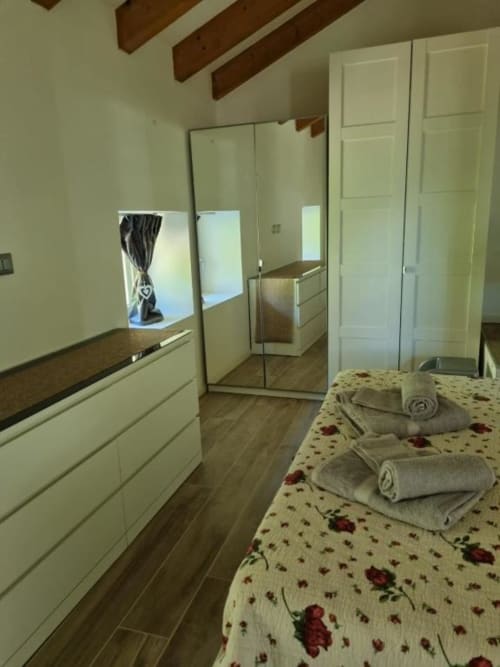 Camera da letto al Maso Kreuzberg B&B di Trento con biancheria floreale, armadio specchiato e travi in legno