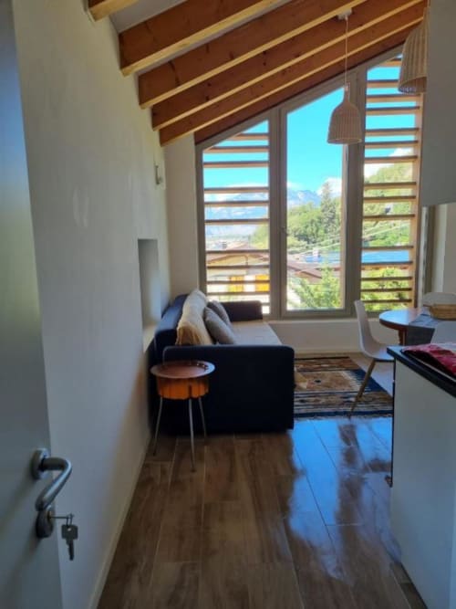 Moderno appartamento a Maso Kreuzberg con vista montagne, travi in legno, divano nero e terrazza con veduta su Trento