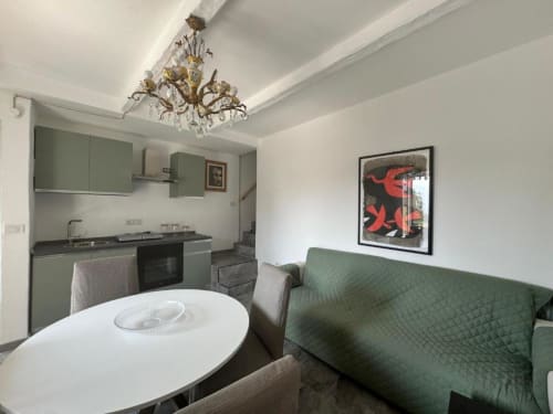 Cucina e zona living moderna nell'appartamento di Sormano con mobili verdi, pareti bianche, lampadario ornamentale e divano letto