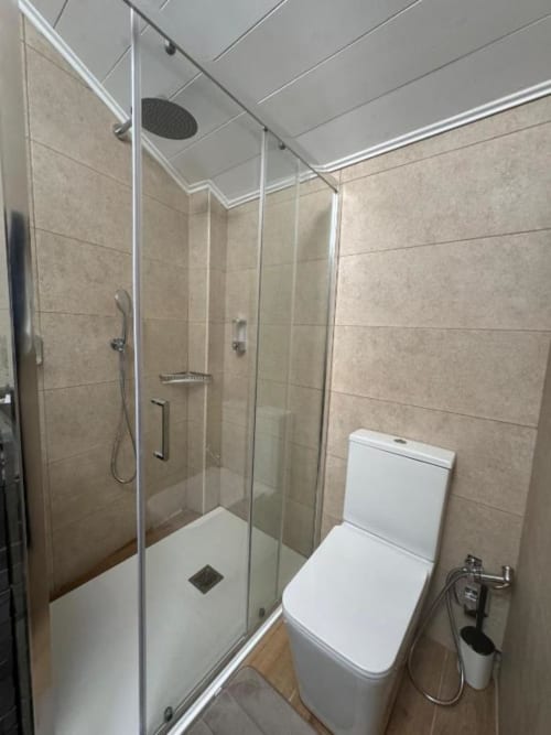 Bagno moderno nell'appartamento di Sormano con doccia in vetro, wc bianco, piastrelle beige e ventilatore di aerazione