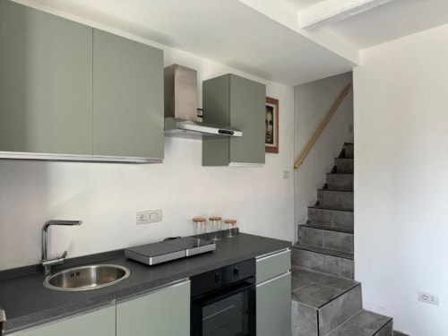 Moderna cucina con mobili verde salvia, piano di lavoro nero e scala nell'appartamento Sormano di THE V Collection hotel