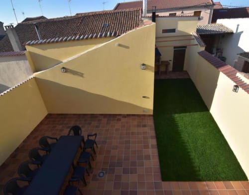 Patio de casita rural tradicional en Nieva con terraza, césped artificial y edificios de paredes amarillas