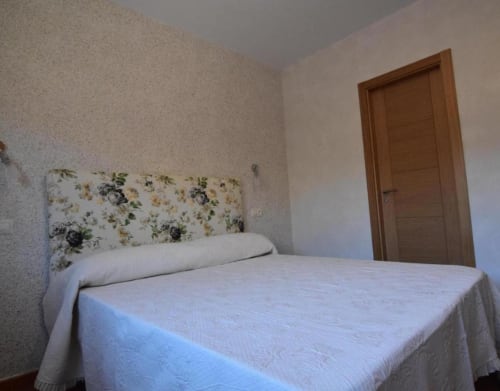 Dormitorio de cabaña en Nieva con ropa de cama blanca, cabecero floral y puerta de madera