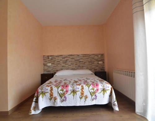 Acogedora habitación de cabaña en Nieva con colcha floral, cabecero de madera rústica, paredes melocotón y luz natural