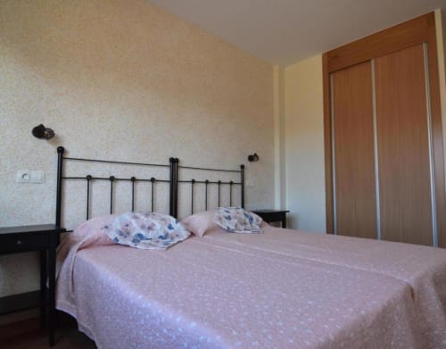 Acogedora habitación de la cabaña Tradición Rural en Nieva con cama de hierro, ropa de cama rosa y armario de madera.