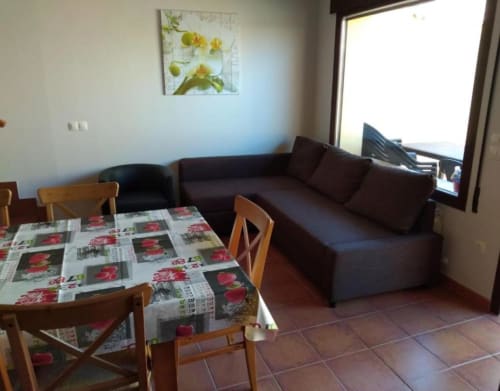 Sala de estar de cabaña con mesa de comedor, sillas de madera, sofá oscuro y cuadro de flores amarillas en Nieva