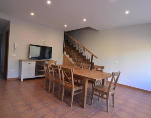 Comedor de cabaña de planta abierta con mesa de madera, piso de baldosas de barro, cocina, TV y escalera en Nieva