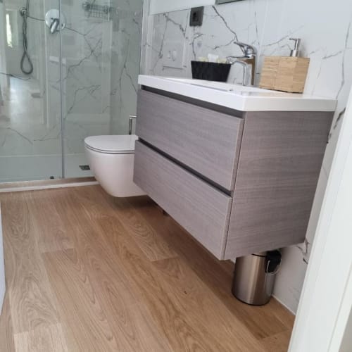 Bagno moderno a Maso Kreuzberg con vanity grigia, lavabo bianco, wc, rivestimento in marmo e pavimento in legno