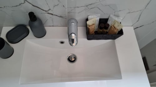 Lavabo moderno della Maso Kreuzberg B&B a Trento con rivestimento in marmo, accessori neri e articoli da toilette.