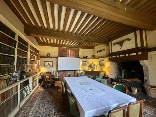 Salle historique de bibliothèque avec plafond à poutres, cheminée et table de conférence au Château de Vaux Morvan