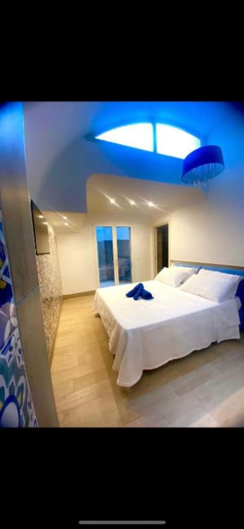 Camera moderna della San Nicola Suite Mini Apartments a Sorrento con letto bianco, lucernario blu, pavimento in legno e vista sul giardino