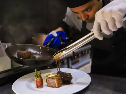 Chef presentando plato de res en el restaurante del Hotel 40 Cañones en Mahahual, con drizzle de salsa y guarnición de espárrago