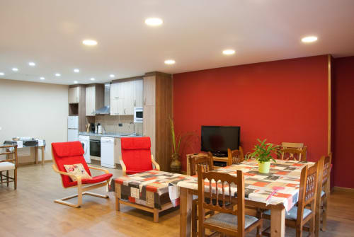 Interior luminoso de cabaña con pared de acento rojo, muebles de madera, mesa de comedor, cocina y sillas rojas en Tradición
