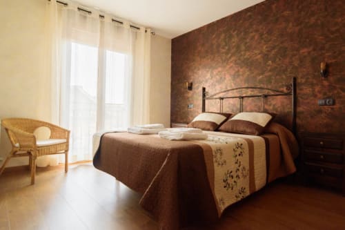 Dormitorio rústico en la cabaña Tradición Rural de Nieva con cama de hierro forjado, paredes texturizadas marrones y vistas al jardín