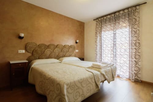 Acogedora habitación de cabaña en Tradición Rural con camas gemelas, cabecero tejido, paredes terracota y cortinas con vista al jardín en Nieva