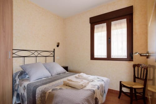 Acogedora habitación de cabaña en Tradición Rural con cama de hierro forjado, almohadas crema, toallas dobladas y vistas al jardín desde madera