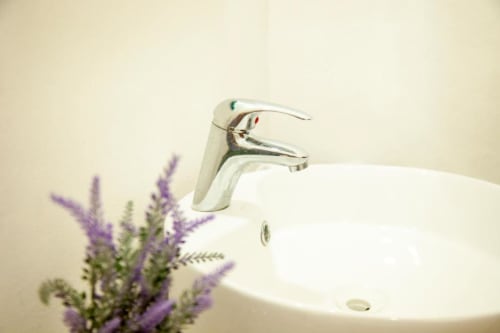 Modern chrome faucet over white sink with purple flowers at La Familia Hotel, San Blas