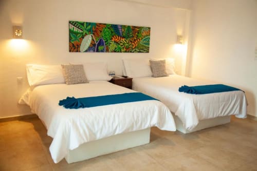 Two queen beds with white linens and blue runners at La Familia Hotel in San Blas, Nayarit, Mexico