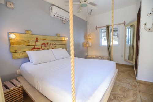 Habitación moderna del Hotel 40 Cañones en Mahahual con cama suspendida por cuerdas, cabecero de madera y diseño contemporáneo luminoso