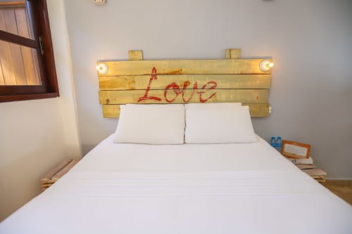 Acogedora habitación del Hotel 40 Cañones en Mahahual con cabecera de madera con texto rojo 'Love' y ropa de cama blanca