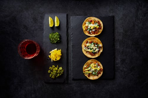 Tres tacos con ingredientes, gajos de lima y cilantro fresco en pizarra negra en Casa Donceles, Ciudad de México