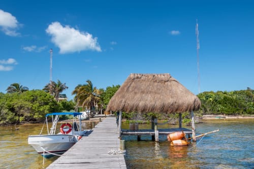 Muelle de madera con bote en Hotel 40 Cañones de Mahahual, México, con palapa de techo de palma y frente tropical