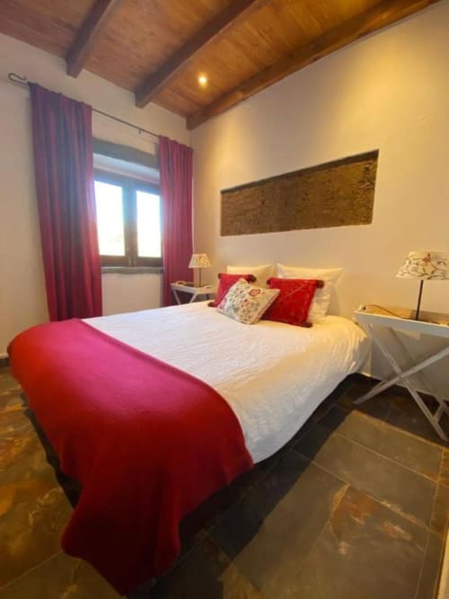 Bedroom in Quim's House villa at Corvatos Casas do Monte with queen bed, red accents, wooden beams, and lake views