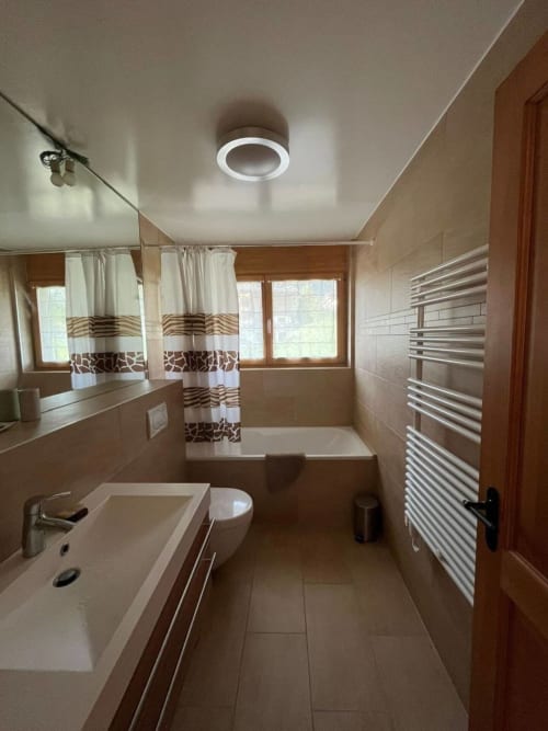 Salle de bain moderne à la Grangette Villars avec lavabo blanc, toilettes, porte-serviettes chauffant, baignoire et rideau à motifs