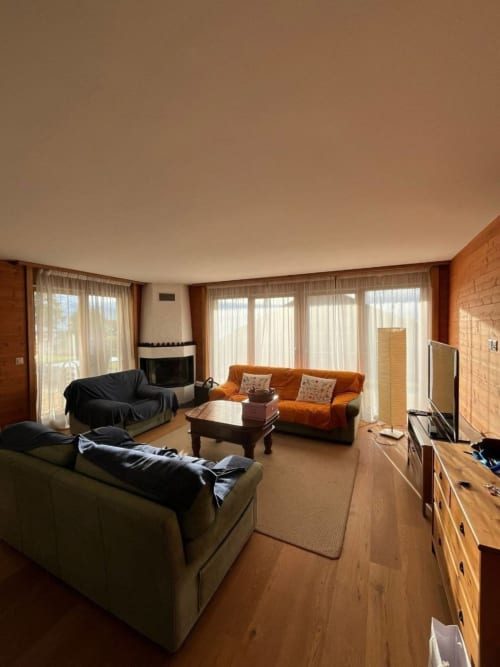 Spacieux salon de Grangette Villars avec canapés beige et orange, foyer, mobilier en bois et vue sur les montagnes