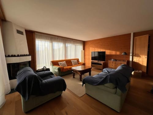Spacieux séjour à Grangette Villars avec deux fauteuils confortables, canapé orange, cheminée et vue montagne
