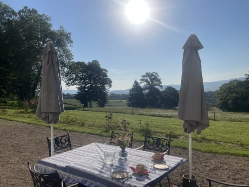 Installation de repas en plein air au Château de Vaux Morvan avec deux parasols, table et vue sur les paysages vallonnés d'Étang sur Arroux,