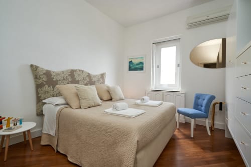 Luminosa camera dell'hotel Wonderful Positano con biancheria beige, testata fantasia, sedia blu, pavimento in legno e montagna