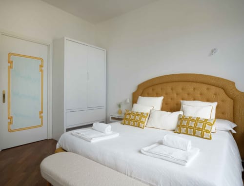 Camera da letto luminosa dell'hotel Wonderful Positano con testata in rattan dorato, biancheria bianca e cuscini geometrici gialli