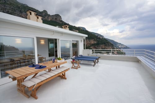 Splendida terrazza di Positano con lettini in legno, vista sul mare e edifici a picco sulla costa amalfitana