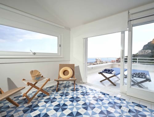 Luminosa camera costiera a Wonderful Positano con pavimento geometrico blu, sedie in legno e vista sul mare dal balcone