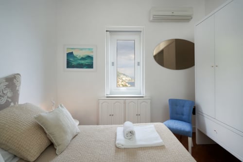 Luminosa camera da letto a Wonderful Positano con vista sul mare, arredamento costiero, arredi bianchi e poltrona blu