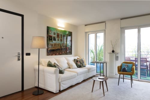 Elegante soggiorno all'appartamento GIRESIO 41 di Milano con divano bianco, lampada a stelo e accesso alla terrazza con vista sulla città.
