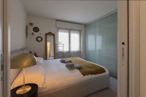 Camera da letto moderna all'appartamento GIRESIO 41 di Milano con letto matrimoniale, lampada in ottone, armadio turchese e accesso al balcone con vista sulla città
