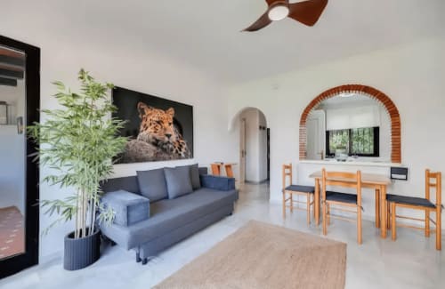 Espacio moderno en SACORO Marbella con sofá azul, sillas de comedor de madera y obra de arte con leopardos