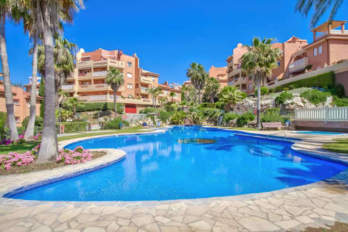 Terraza de piscina de lujo en apartamentos SACORO de Marbella con palmeras, flores rosas y vistas al mar